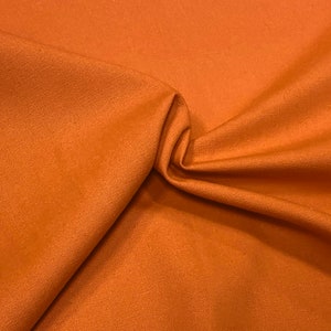 May include: A close-up of a rust-colored fabric with a smooth, woven texture. The fabric is folded and draped, showcasing its soft, pliable nature.