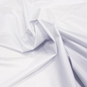 May include: White fabric with a smooth, silky texture. The fabric is folded and draped, creating soft folds and curves.