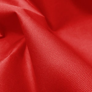May include: Close-up of a red fabric with a textured surface. The fabric is folded and has a soft, smooth feel.