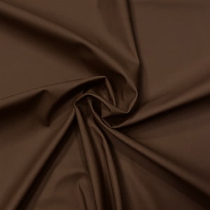 May include: A close-up of a smooth, brown fabric with a soft, flowing texture. The fabric is draped and folded, creating a sense of movement and depth.