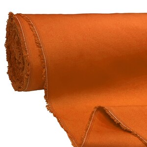 May include: A roll of orange fabric with a fringed edge. The fabric is rolled up and the end is unfurled, showing the texture of the material.
