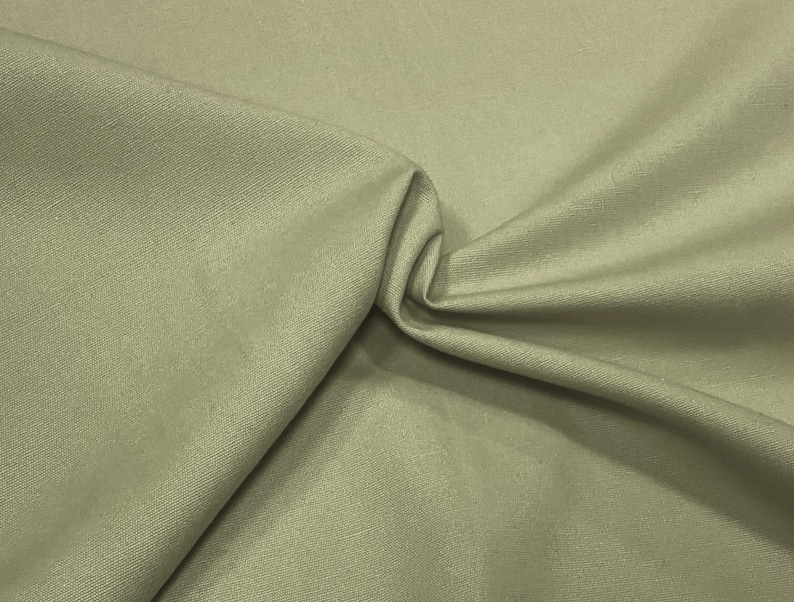 May include: A close-up of a light beige fabric with a subtle texture. The fabric is folded and draped, showcasing its soft and smooth surface.