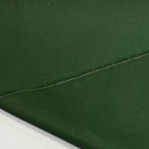 May include: Close-up of a dark green fabric with a raw edge and a single seam. The fabric has a subtle texture and a slightly rough feel.