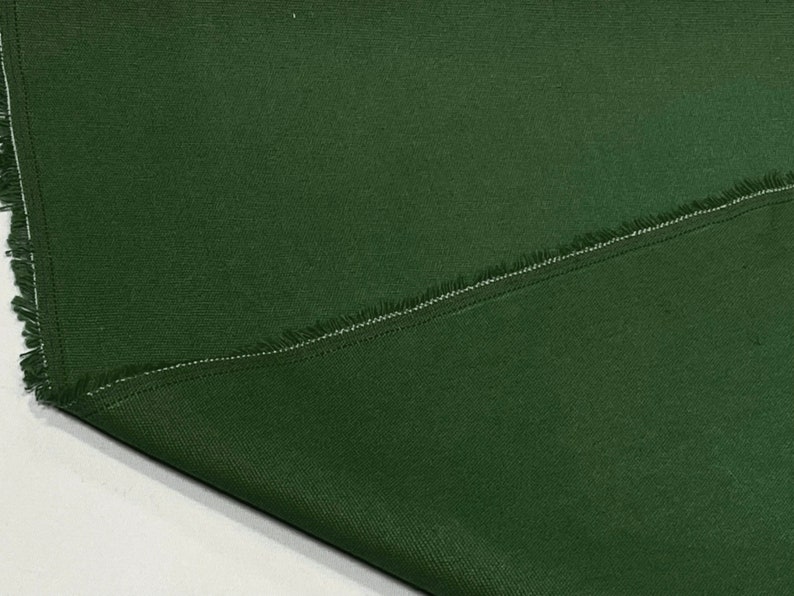 May include: Close-up of a dark green fabric with a raw edge and a single seam. The fabric has a subtle texture and a slightly rough feel.