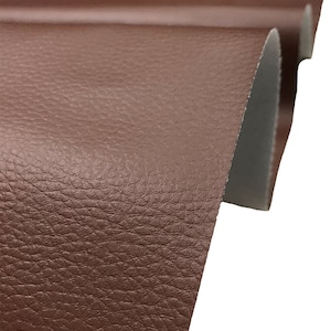 May include: Close-up of a brown faux leather fabric with a textured surface. The fabric is folded over on itself, showing the underside.