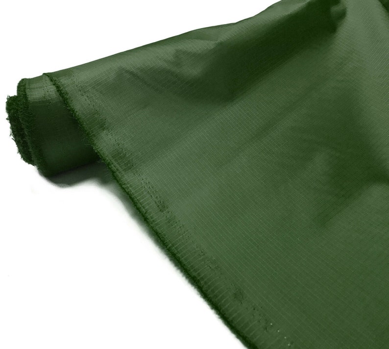 May include: A roll of dark green fabric with a textured surface. The fabric is folded and rolled up, with the edges visible.