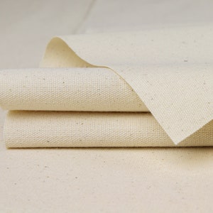 May include: Close-up of three layers of natural white canvas fabric folded together. The fabric has a subtle texture and a slightly off-white color.