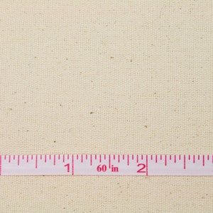 May include: A close-up of a plain, off-white canvas fabric with a pink measuring tape laid across it. The tape reads "60 in" and has markings for 0, 1, 2, and 3 inches.