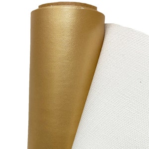 May include: A roll of gold faux leather fabric with a textured surface. The fabric is rolled up and a white canvas fabric is visible behind it.