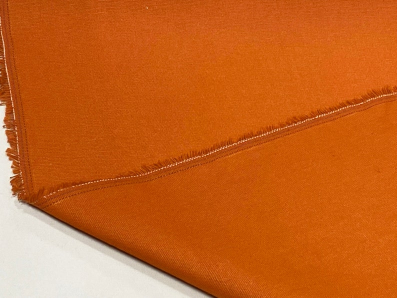 May include: A close-up of a folded piece of burnt orange fabric with a raw edge. The fabric has a subtle texture and a slight sheen.