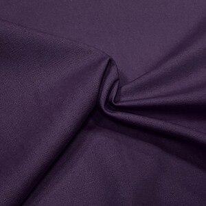 May include: A close-up of a deep purple fabric with a textured weave. The fabric is folded and draped, showing its soft and smooth texture.