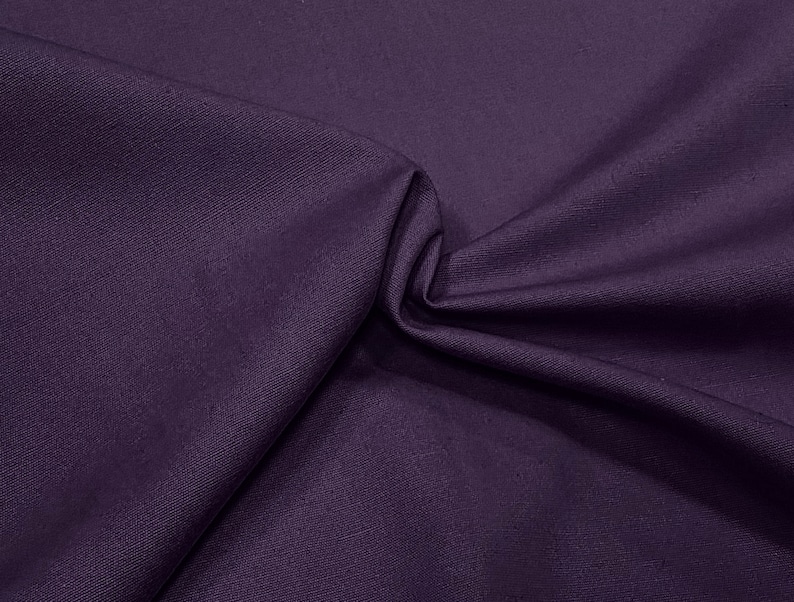 May include: A close-up of a deep purple fabric with a textured weave. The fabric is folded and draped, showing its soft and smooth texture.