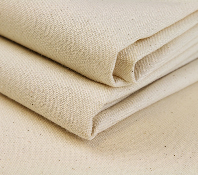 May include: Close-up of a folded piece of natural-colored canvas fabric. The fabric has a woven texture and is folded in thirds.