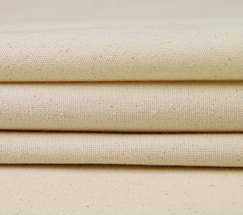 May include: Close-up of a stack of natural-colored canvas fabric. The fabric has a woven texture and a slightly rough surface.