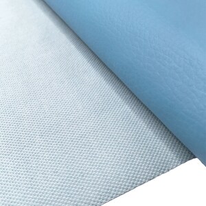 May include: A close-up of a light blue fabric with a textured surface. The fabric is folded over to reveal a white backing with a grid pattern.
