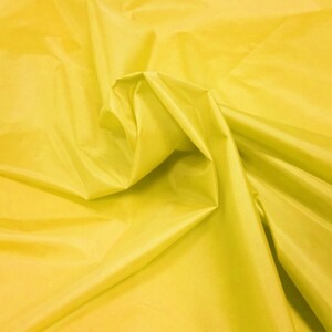 May include: A bright yellow fabric with a smooth, silky texture. The fabric is folded and draped, showcasing its soft, flowing quality.
