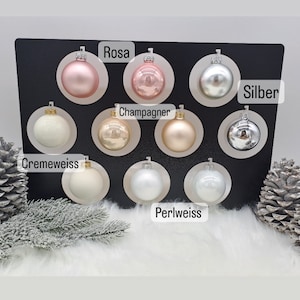 Pode incluir: Conjunto de 10 enfeites de Natal em v&aacute;rias cores, incluindo prata, champanhe, creme, branco p&eacute;rola e rosa. Os enfeites s&atilde;o exibidos em um fundo preto com os nomes das cores escritos abaixo de cada enfeite.