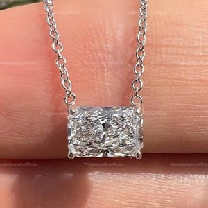 May include: A silver necklace with a rectangular diamond pendant. The diamond is set in a silver bezel and suspended from a delicate silver chain. The pendant is about 1.3 cm long, displaying a brilliant, multifaceted surface, reflecting light.