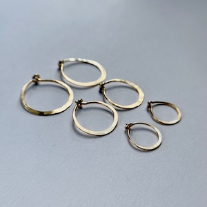 May include: Five gold hoop earrings of varying sizes. The earrings are all made of a hammered metal and have a shiny finish.