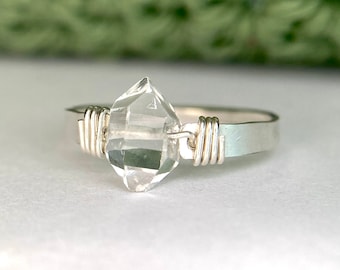May include: A silver ring with a clear quartz crystal set in the centre. The crystal is faceted and has a geometric shape. The ring is made of wire wrapped around the band.
