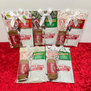 Puede incluir: Seis bolsas de regalo con temática navideña llenas de una variedad de artículos, que incluyen bolsitas de té, bastones de caramelo, galletas y cucharas. Las bolsas están decoradas con patrones festivos y cintas.
