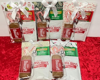 May include: Six Christmas-themed gift bags filled with a variety of items, including tea bags, candy canes, cookies, and spoons. The bags are decorated with festive patterns and ribbons.