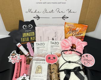 May include: A gift box filled with self-care items. Includes a black bat-shaped face mask, Tazo Pumpkin Spice Chai tea bags, a pink scrunchie, and a white plush eye mask with a black bow. Halloween-themed stickers and a lip balm are also included.