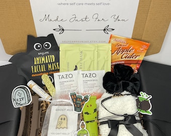 May include: A Halloween-themed gift box filled with self-care items. Includes a black cat face mask, Tazo Pumpkin Spice Chai tea bags, Alpine Spiced Apple Cider, a white plush item with a black bow, and stickers. The box reads "SelfCare Sunday".