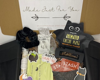 May include: A brown cardboard box filled with Halloween-themed self-care items. The box has a white label with the text "Self Care Sun Jay" and "Made Just For You". The items include a black velvet scrunchie, a ghost-shaped tag, a black bat-shaped face mask, a gold eye mask, a black hair clip, a bottle of bath salts, a tea bag, and a black cat sticker.