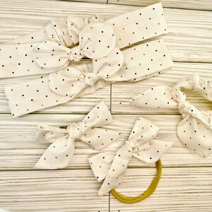 May include: A set of five hair accessories featuring a white fabric with colorful polka dots. The set includes three headbands, one scrunchie, and one hair tie.
