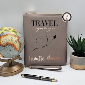 Könnte beinhalten: Ein taupefarbener Reiseorganizer mit den Aufschriften "TRAVEL ORGANIZER" und "Familie Meier", ein Globus, ein Stift und eine kleine Topfpflanze. Der Organizer hat einen Reißverschluss und eine Handschlaufe.