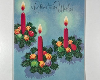 May include: A vintage Christmas card with the text "Christmas Wishes" printed in black script. The card features three red candles with flames, each surrounded by a wreath of green pine branches and colorful ornaments.