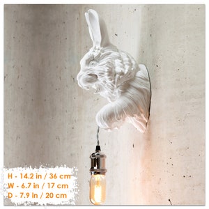 May include: White ceramic rabbit wall lamp with a hanging light bulb. The lamp is 14.2 inches tall, 6.7 inches wide, and 7.9 inches deep.