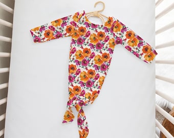 Puede incluir: Una bata de bebé blanca con mangas largas y un fondo anudado. La bata presenta un estampado floral con flores naranjas, rosas y amarillas.