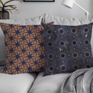 May include: Two decorative throw pillows with geometric patterns. One pillow features a navy blue background with a gold sunburst design. The other pillow has a brown background with a navy blue starburst design.