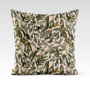 Op de afbeelding: Een decoratief kussen met een cr&egrave;mekleurige achtergrond en een abstract bloemenpatroon in groen en bruin.