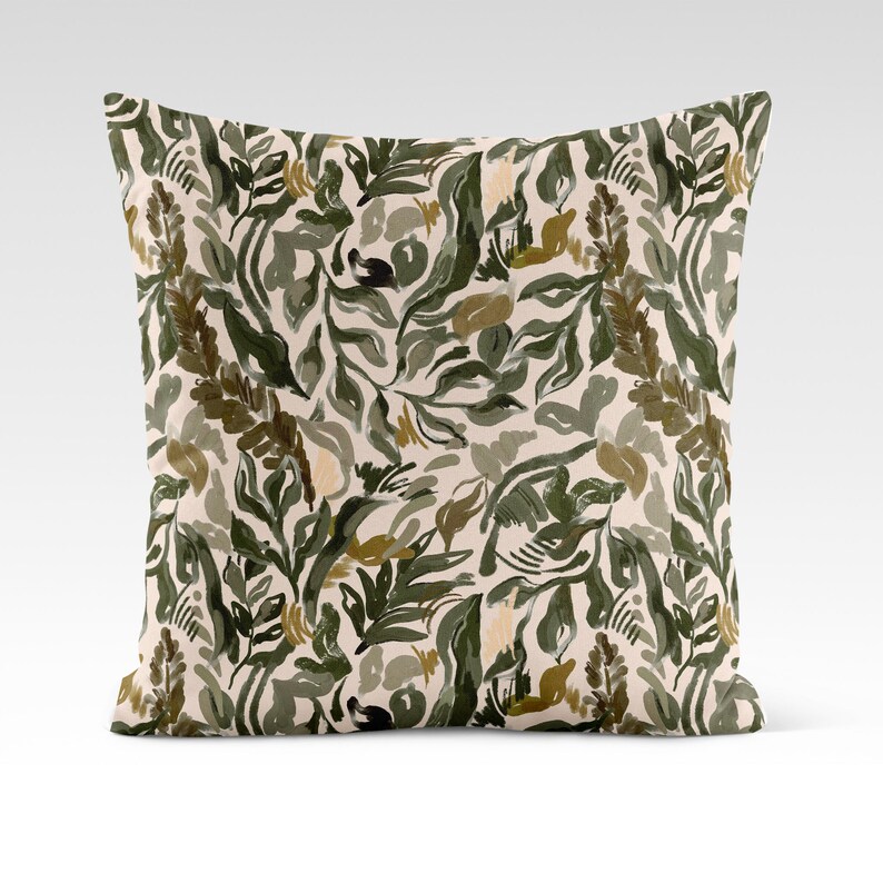 Op de afbeelding: Een decoratief kussen met een cr&egrave;mekleurige achtergrond en een abstract bloemenpatroon in groen en bruin.