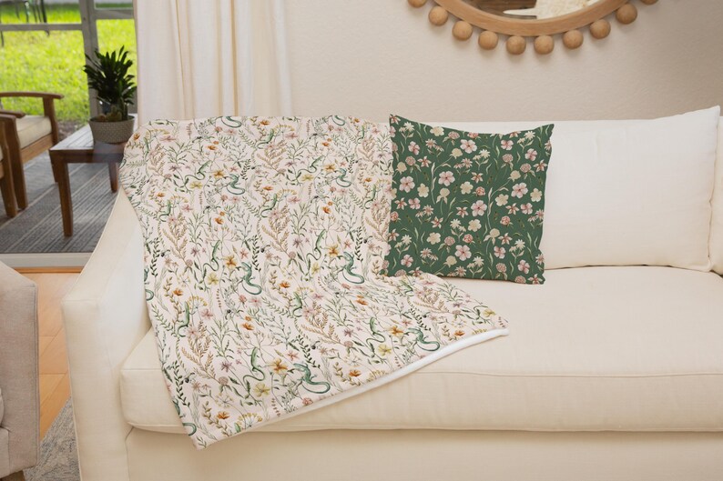 May include: A white throw blanket with a floral and snake pattern is draped over a white couch. A green throw pillow with a floral pattern is on the couch.