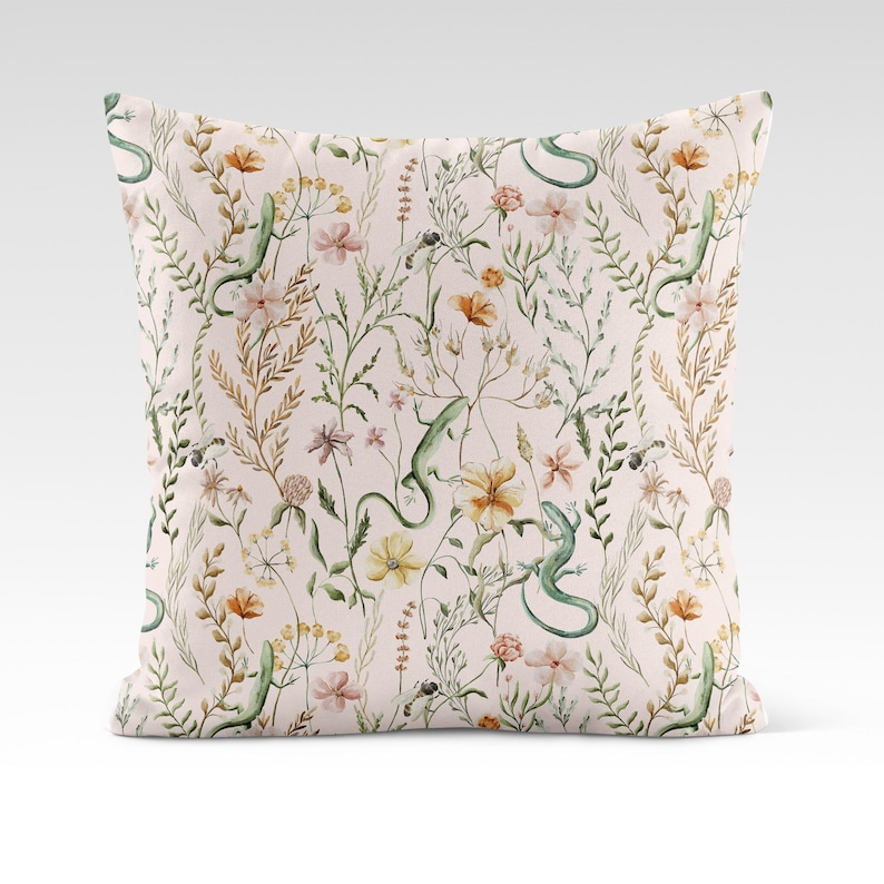 May include: A pink throw pillow with a floral pattern featuring green lizards, yellow, orange, and pink flowers, and green leaves.