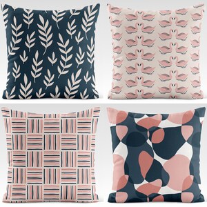 May include: Four decorative throw pillows with different patterns. One pillow features white leaf designs on a navy blue background. Another has a pattern of pink swans on a beige background. A third pillow has a grid pattern of pink, navy, and beige stripes. The last pillow has an abstract design of pink and navy shapes.