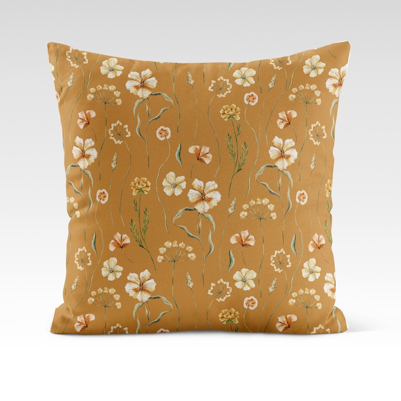 May include: A mustard yellow throw pillow with a white floral pattern. The pillow features a repeating pattern of small white flowers with green stems and leaves.