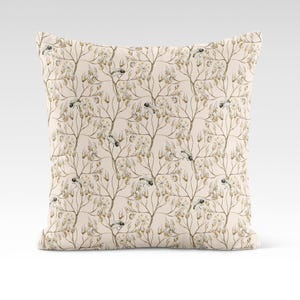 May include: A beige throw pillow with a delicate floral pattern featuring small brown birds and branches. The pillow has a subtle cream background and a soft, textured fabric.