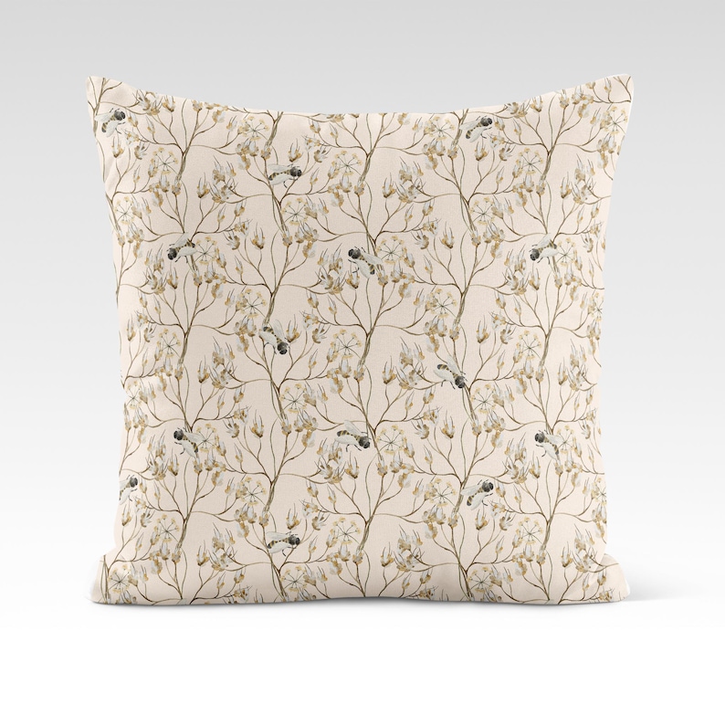 May include: A beige throw pillow with a delicate floral pattern featuring small brown birds and branches. The pillow has a subtle cream background and a soft, textured fabric.
