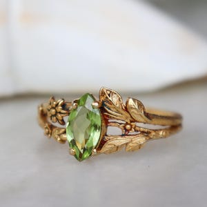 Op de afbeelding: Een gouden ring met een groene edelsteen gezet in een blad- en bloemmotief.