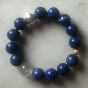 Könnte beinhalten: Ein blaues Edelstein-Armband mit silbernen und goldenen Akzenten. Das Armband besteht aus runden Perlen und hat eine klare Kristallperle.