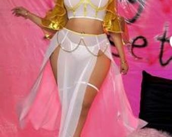 Puede incluir: Un disfraz de danza del vientre blanco y dorado con una falda transparente y un top enjoyado. El disfraz incluye un sujetador con ribete dorado, una falda transparente con aberturas altas y mangas doradas. La modelo lleva sandalias doradas.