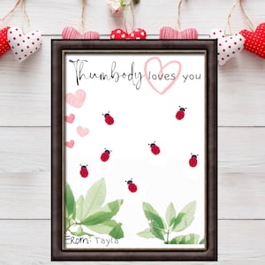 Op de afbeelding: Een ingelijste witte kaart met de tekst "Thumbody loves you" in zwarte cursieve letters. Er staan roze harten en rode lieveheersbeestjes op de kaart. De kaart is ondertekend met "From: Tayla".