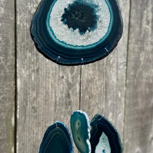 May include: A teal blue agate wind chime with four pieces of agate hanging from a copper wire. The largest piece is round and the other three are oval shaped.