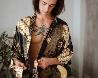 May include: A black and gold patterned silk robe with a long sleeve and a sash tie. The robe is open and the person wearing it is showing their chest and a tattoo.