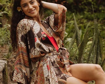 May include: A brown and cream patterned kimono robe with wide sleeves and a matching waist tie, worn over a solid red garment. The robe features a detailed graphic print with repeating shapes and lines throughout the fabric.